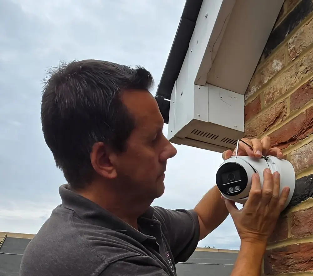 A CCTV camera being aligned by hand on site in Kent, set under the eaves against the brickwork