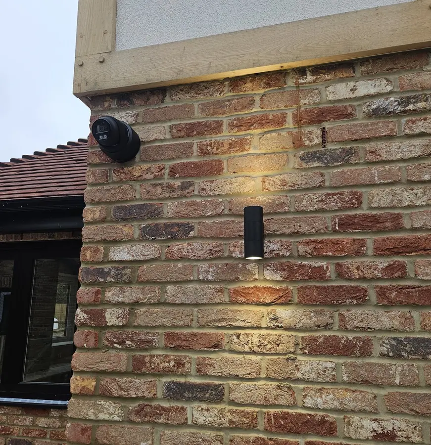 A CCTV camera fitted flush to the brickwork beside the exterior lighting on a Kent home, positioned to look like part of the building rather than an afterthought