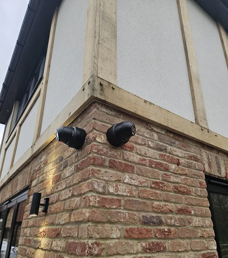 Two CCTV cameras mounted tight under the oak frame on the corner of a Kent home, covering both elevations without standing out against the brickwork